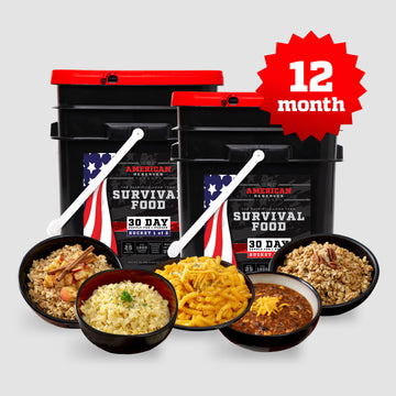 Two black 30 Day survival food buckets by American Reserves feature American flag designs and include freeze-dried emergency meals with rice, macaroni, chili, and oats. A red 12 month starburst highlights a 25-year shelf-life. White spoons are placed in front.