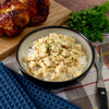 A bowl of rice topped with seasoned Chicken sits invitingly, while American Reserves Protein Bucket rests on a board, perfect for lasting prepared meals. All set amid a plaid cloth, blue napkin, and fork.